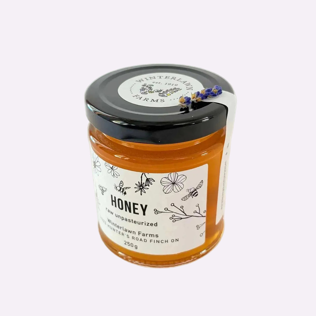 A glass jar of Winterlawn Farms raw unpasteurized honey with a black lid and white label, set against a plain white background.