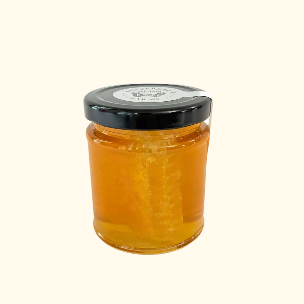 A small glass jar filled with golden amber honey, featuring a black screw-on lid and a white circular Winterlawn Farms label on top