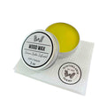 A 2 oz silver tin of Winterlawn Farms Lemon Balm Infused Wood Wax, shown open with the lid beside it on a white textured paper towel. The wood wax inside is a bright yellow-green color.
