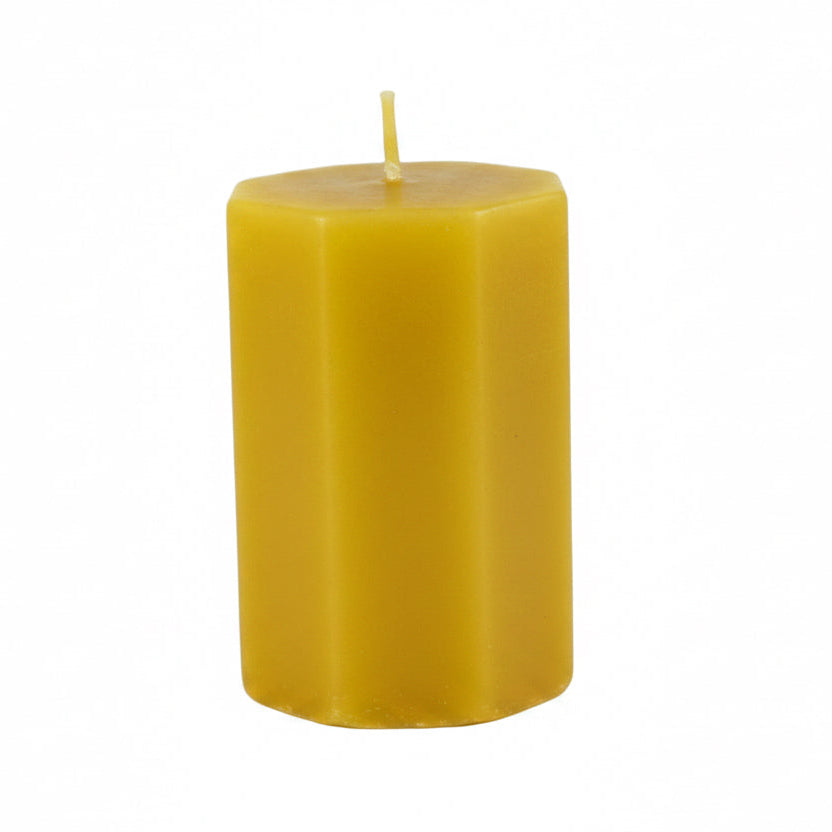 A single yellow hexagonal pillar candle with a short wick, standing upright on a light gray background.