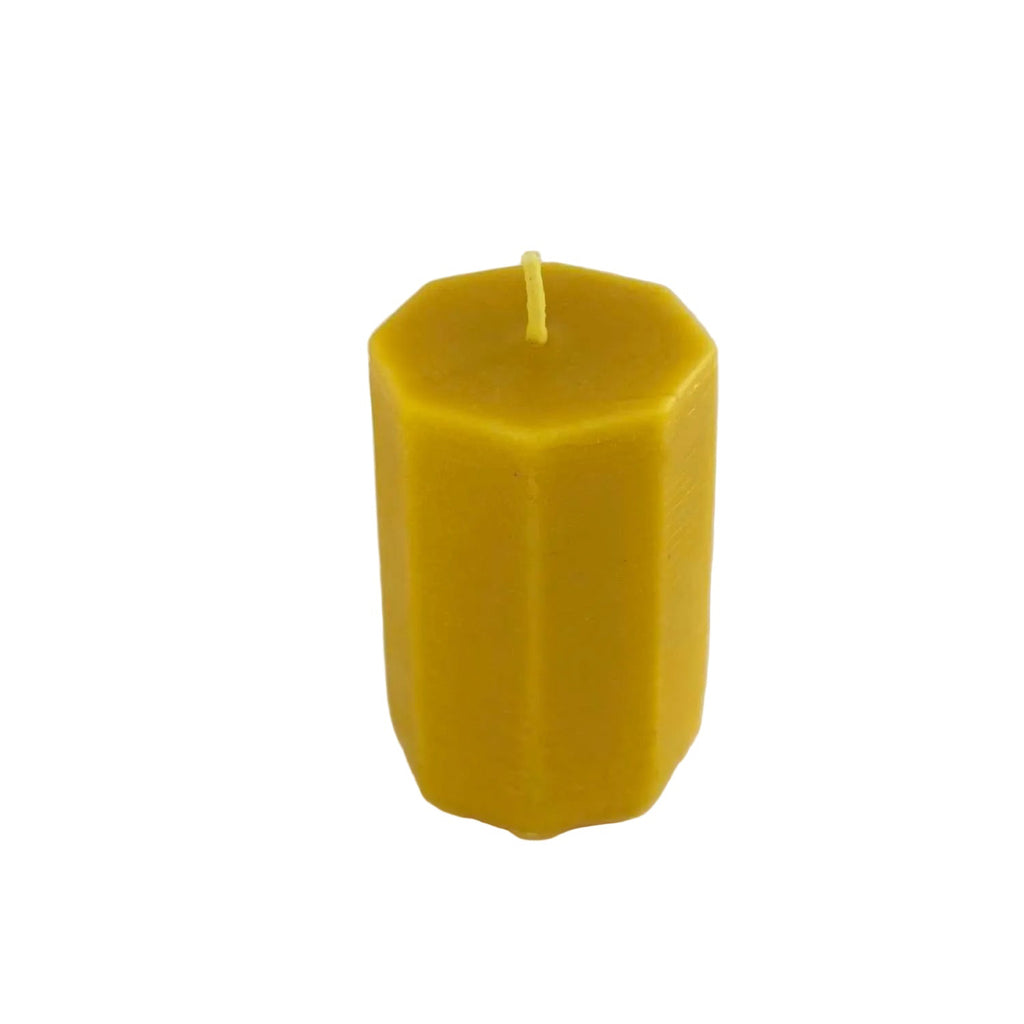 A yellow hexagonal beeswax candle with a single wick, standing upright on a light gray background.