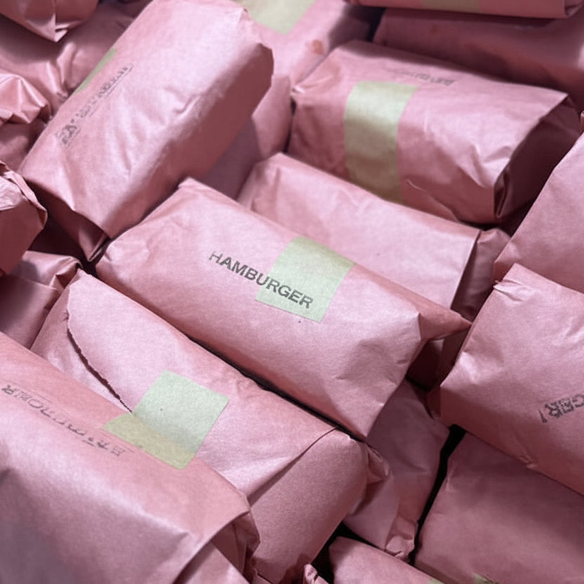 A pile of items wrapped in dusty pink paper and secured with light green tape, filling the frame.