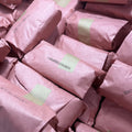A pile of items wrapped in dusty pink paper and secured with light green tape, filling the frame.