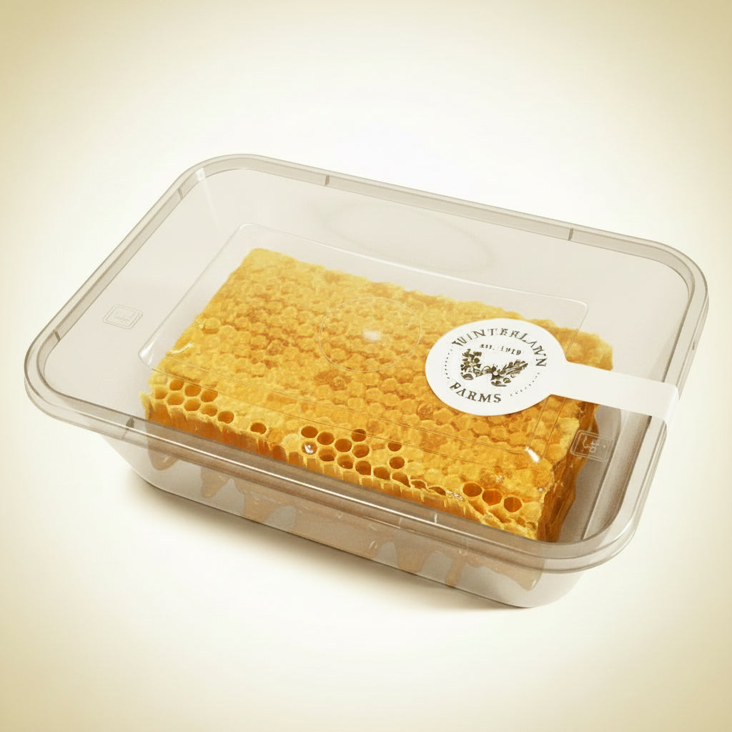 A clear plastic container holding a rectangular piece of honeycomb with visible honey pools in the cells, sealed with a white paper label that reads 'Winter Honey' and 'Winter Farm'.