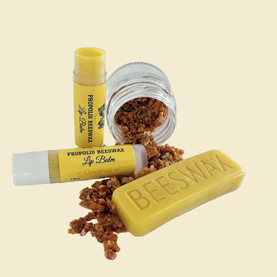 Two yellow lip balm tubes and a yellow bar of beeswax with loose brown beeswax granules, displayed on a clean white background.