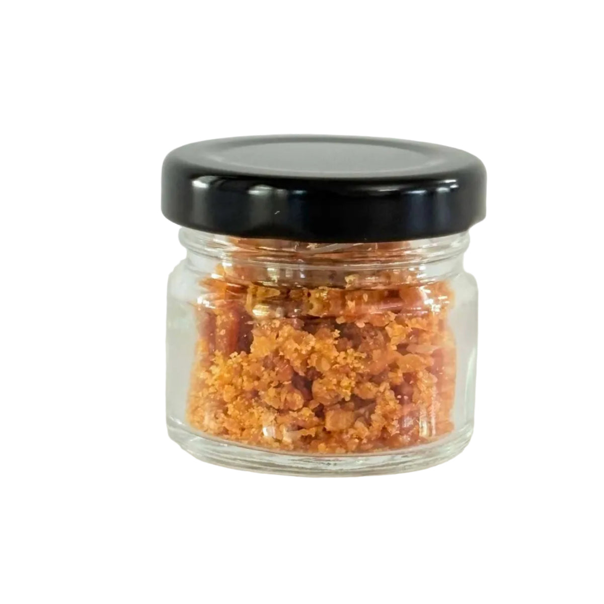 A small clear glass jar filled with coarse orange-brown crystals or salt, sealed with a black screw-top lid, centered on a plain light background.