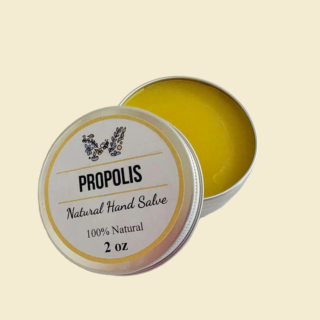A 2 oz silver tin of natural hand salve with its lid off, showing the yellow balm inside. The lid features a white label with black text reading 'PROPOLIS Natural Hand Salve 100% Natural 2 oz' and a small botanical illustration.